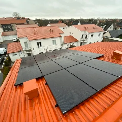Helsvarta solpaneler monterade på ett tak med röda takpannor i ett bostadsområde