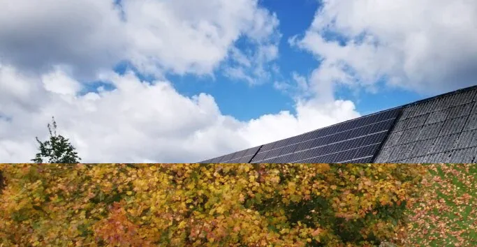 Solpaneler i rader på ett lutande tak mot en himmel med vita moln